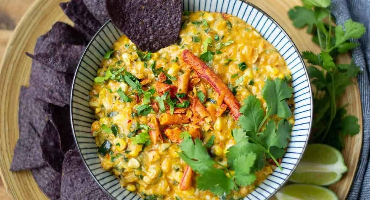 Overhead image of grilled orn dip with poblano peppers in a small bowl with blue corn tortilla chips.