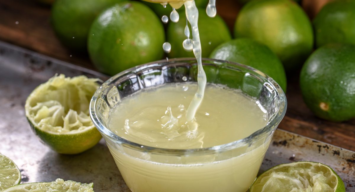 Up close image of lime juice with limes in the background.