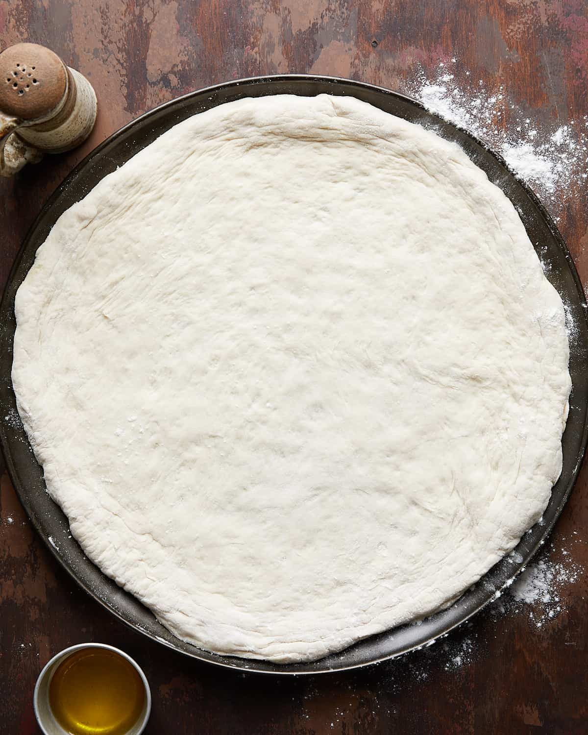 72 hour pizza dough stretched out on a pizza pan on brown background.
