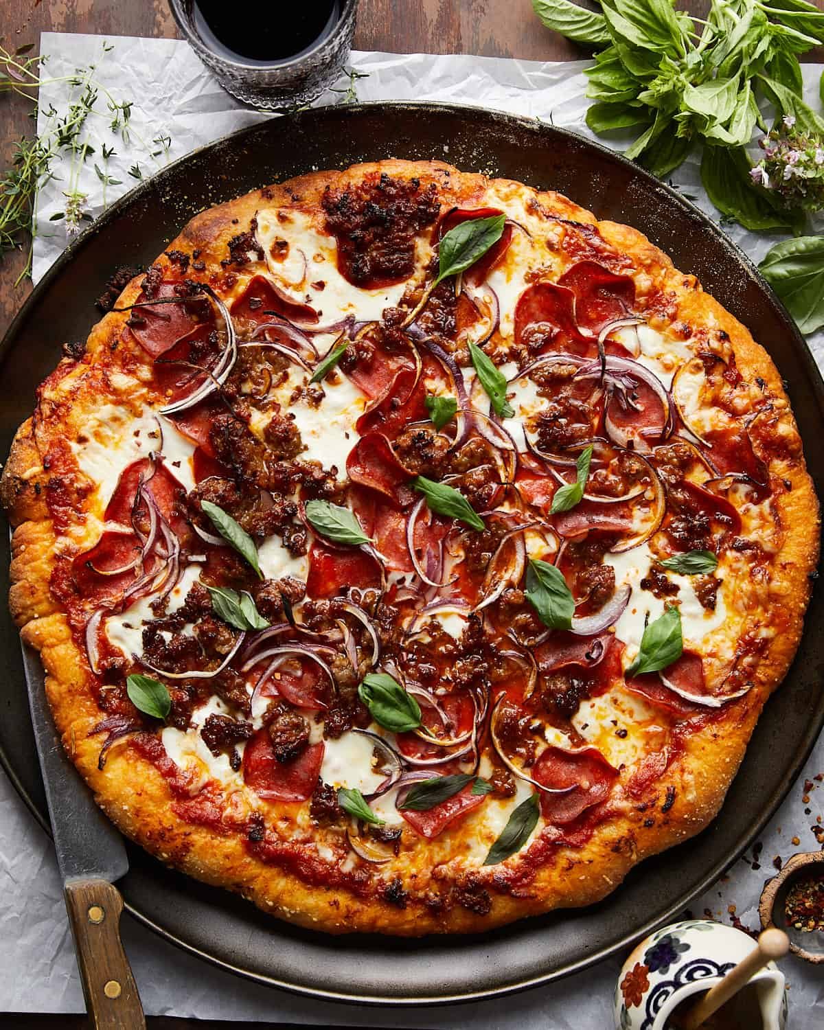 Pizza with pepperoni, sausage, onions, and basil on a pizza pan.