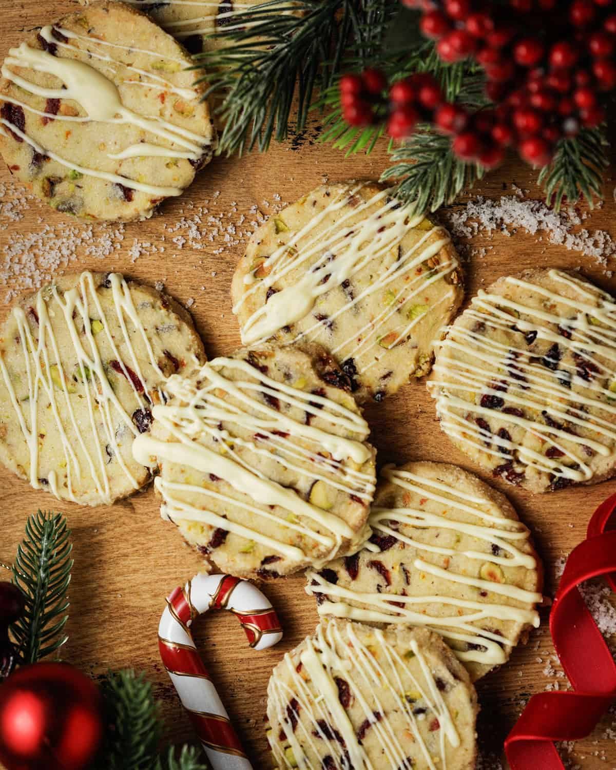 Overhead image of cranberry pistachio shortbread cookies with white chocolate drizzle. Surrounded by Christmas decor.