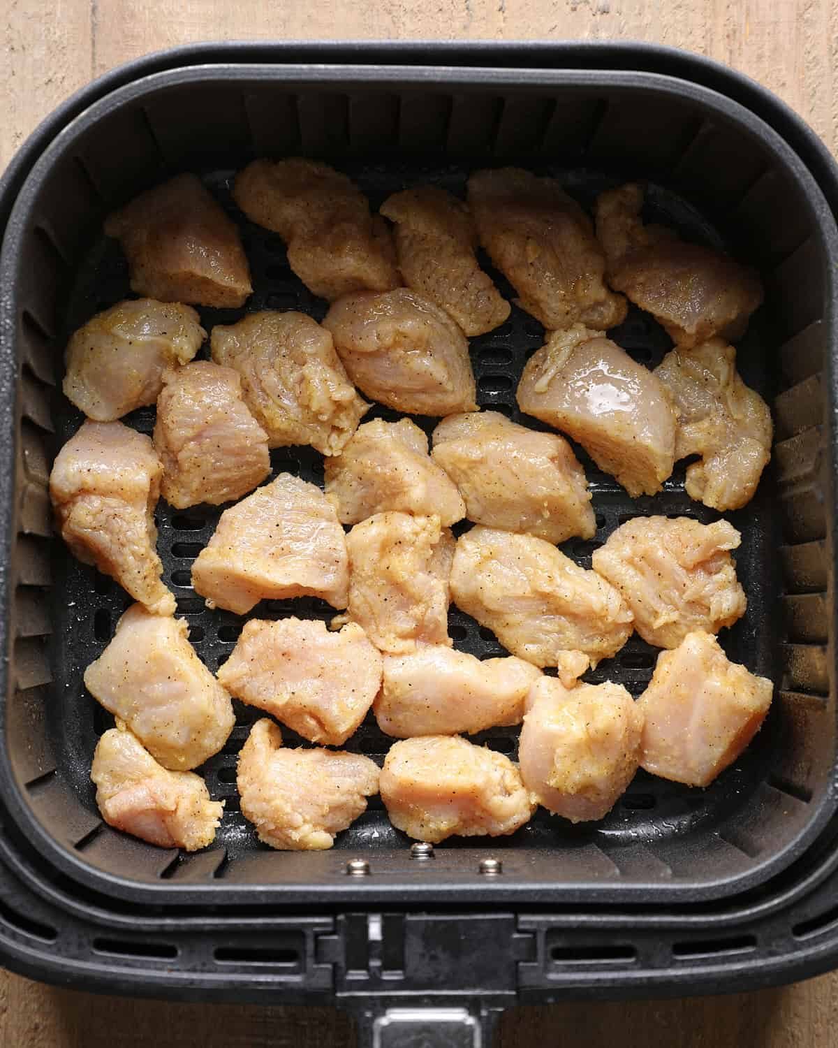 Coated chicken breast pieces arranged in an air fryer basket before cooking.