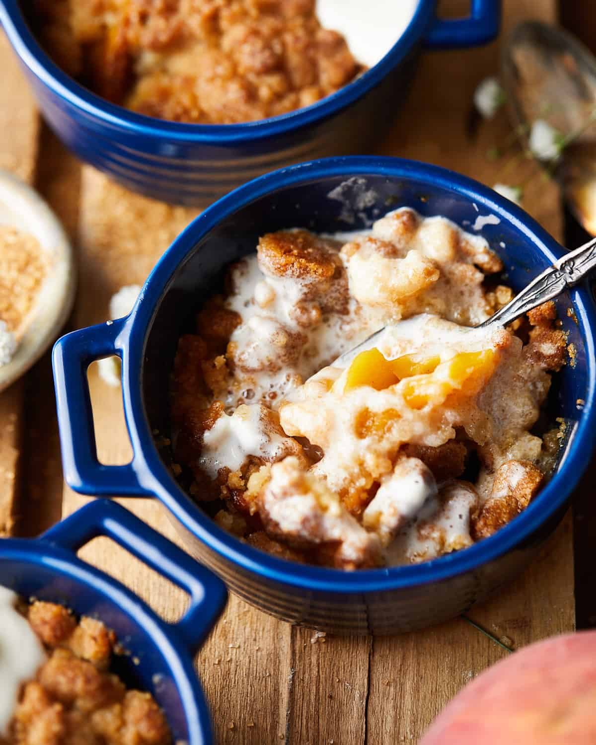 Spoon breaking into air fryer peach cobbler with whipped cream.