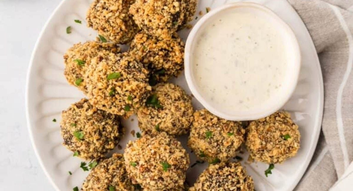 Overhead image of almond crusted mushrooms on white dish with dip on the side.