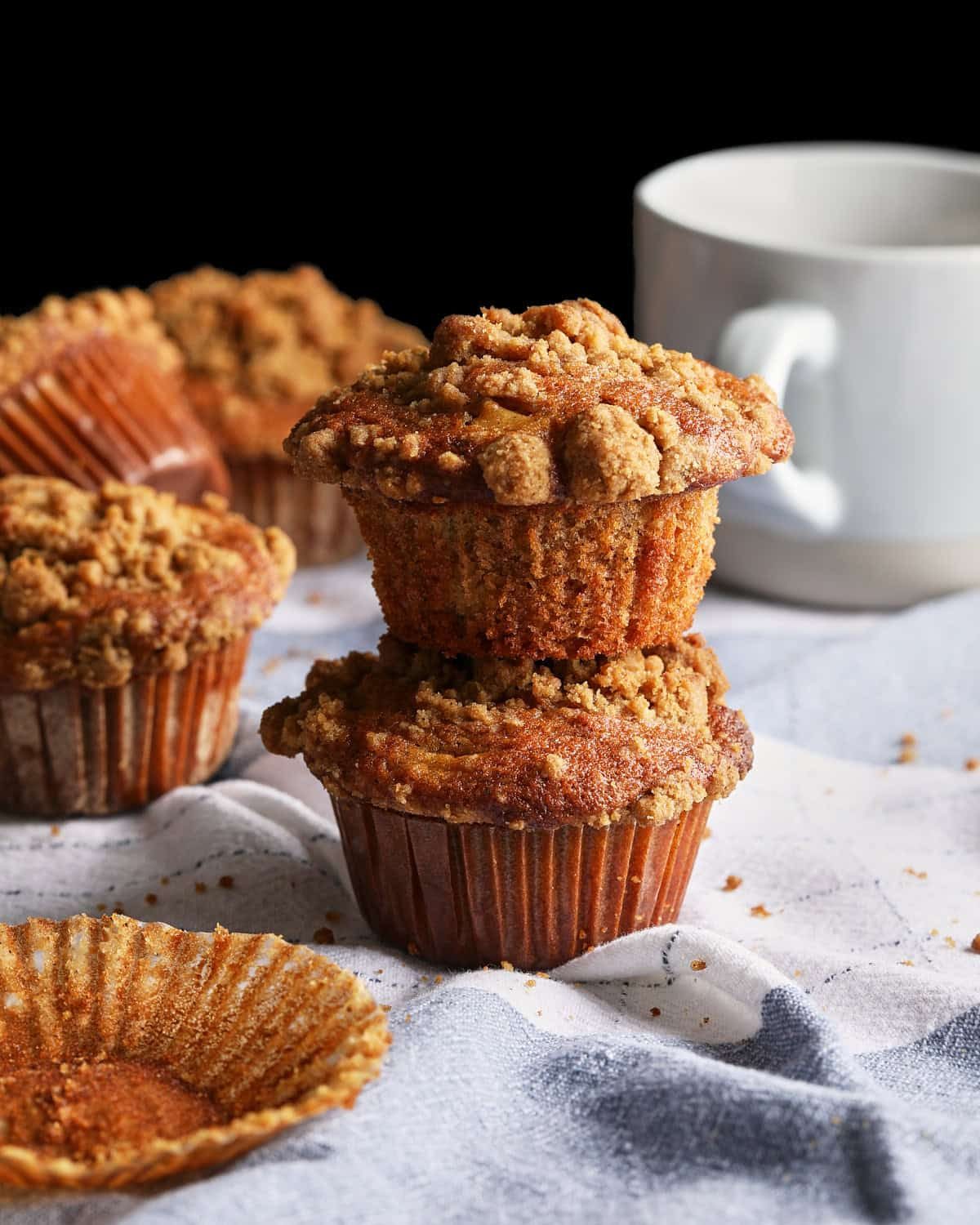 Apple cider muffins stacked 2 high with apple cider in a mug in the background