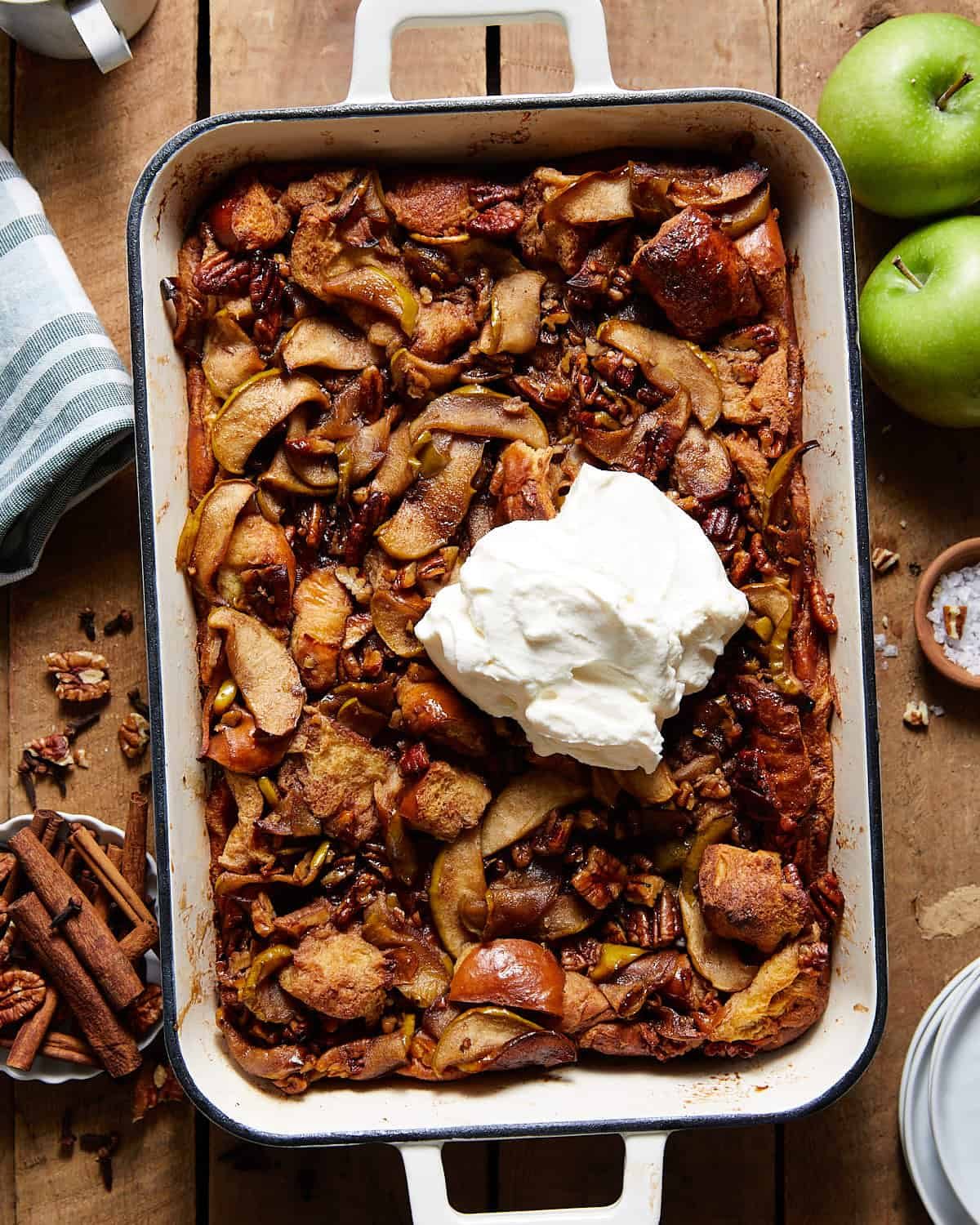 Apple bread pudding in a white casserole dish with whipped cream on top.
