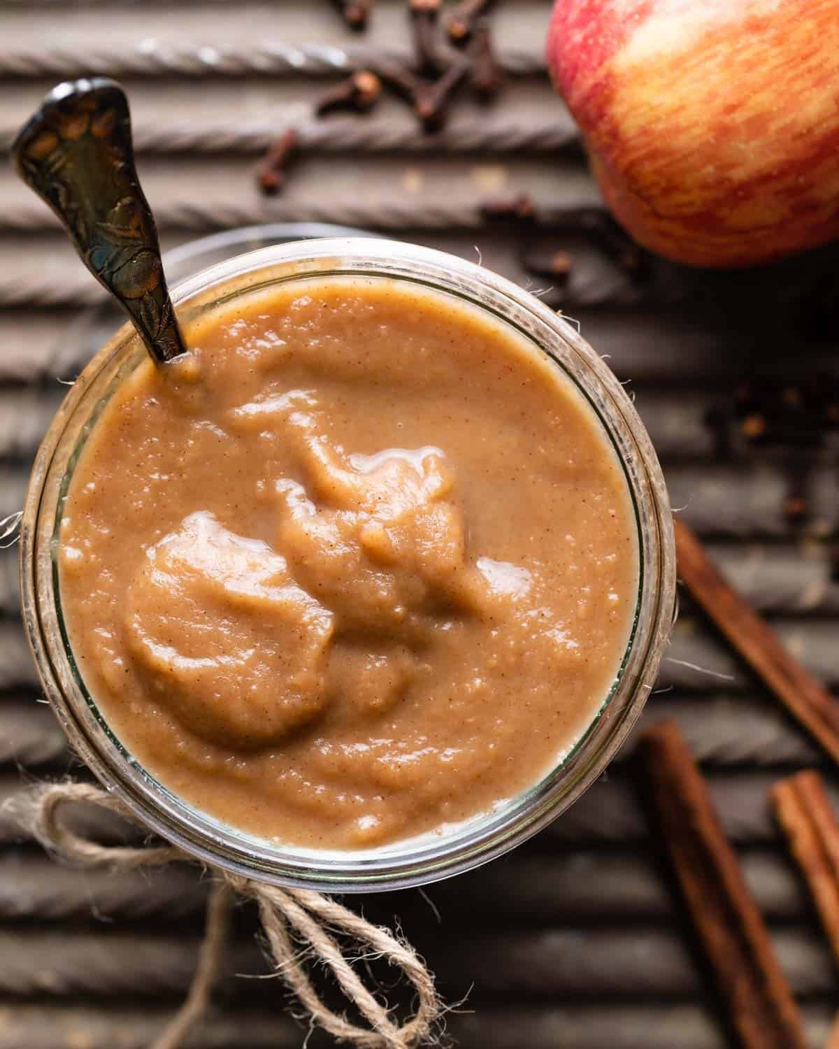 A jar filled with apple curd with a spoon in it.