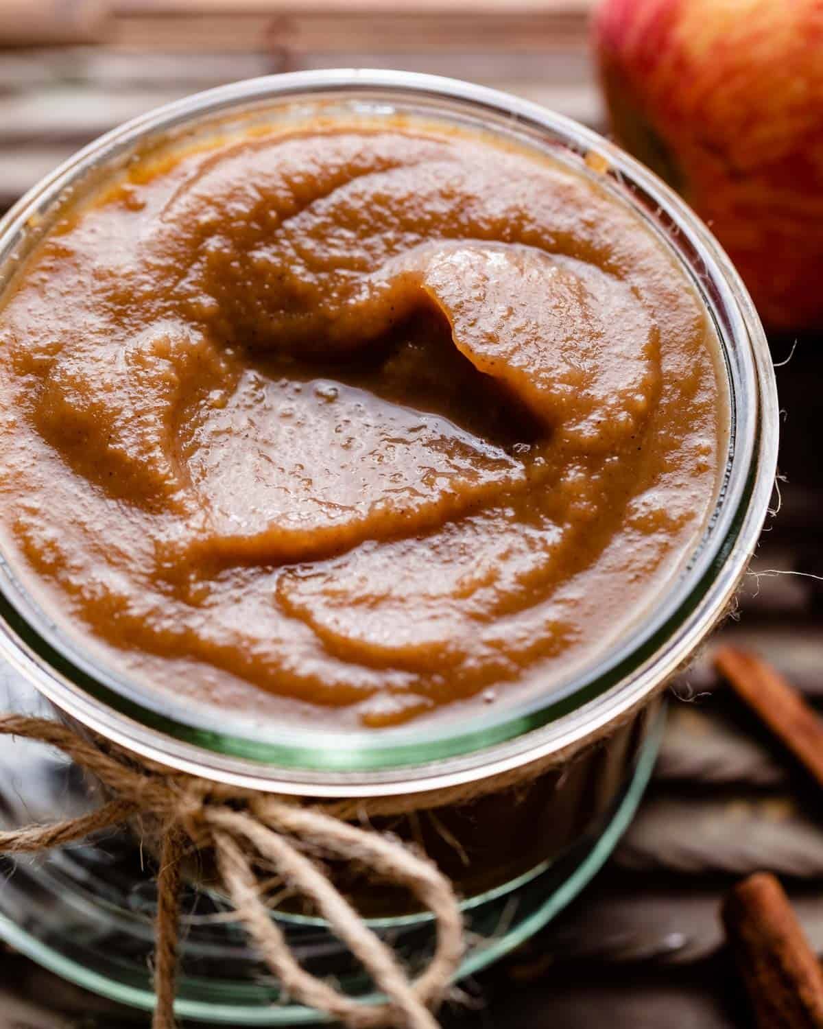 Up close view of apple curd in a glass jar with apples and cinnamon in the background.