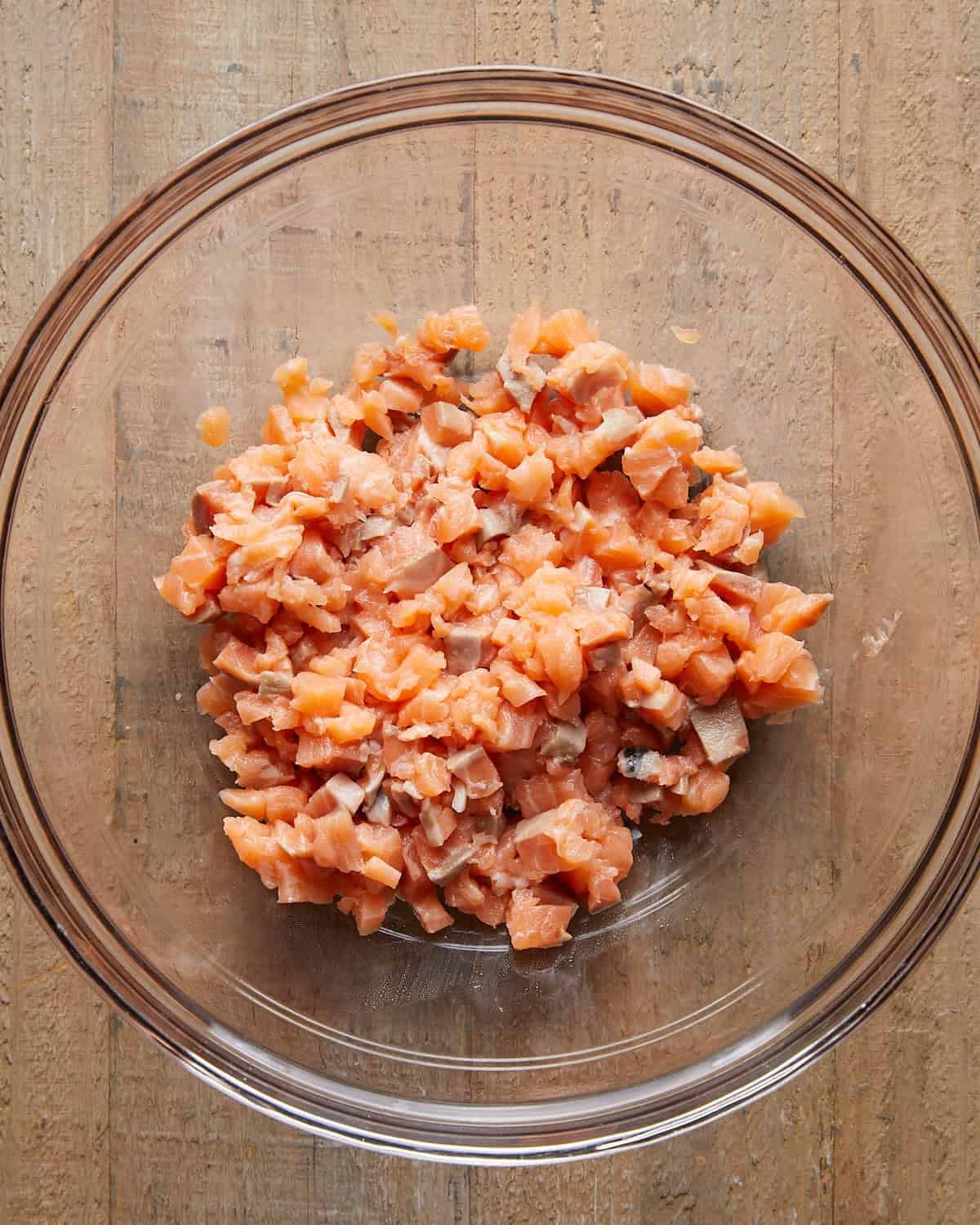 Overhead close-up of finely chopped fresh salmon in a mixing bowl, ready to be mixed for Asian salmon burgers