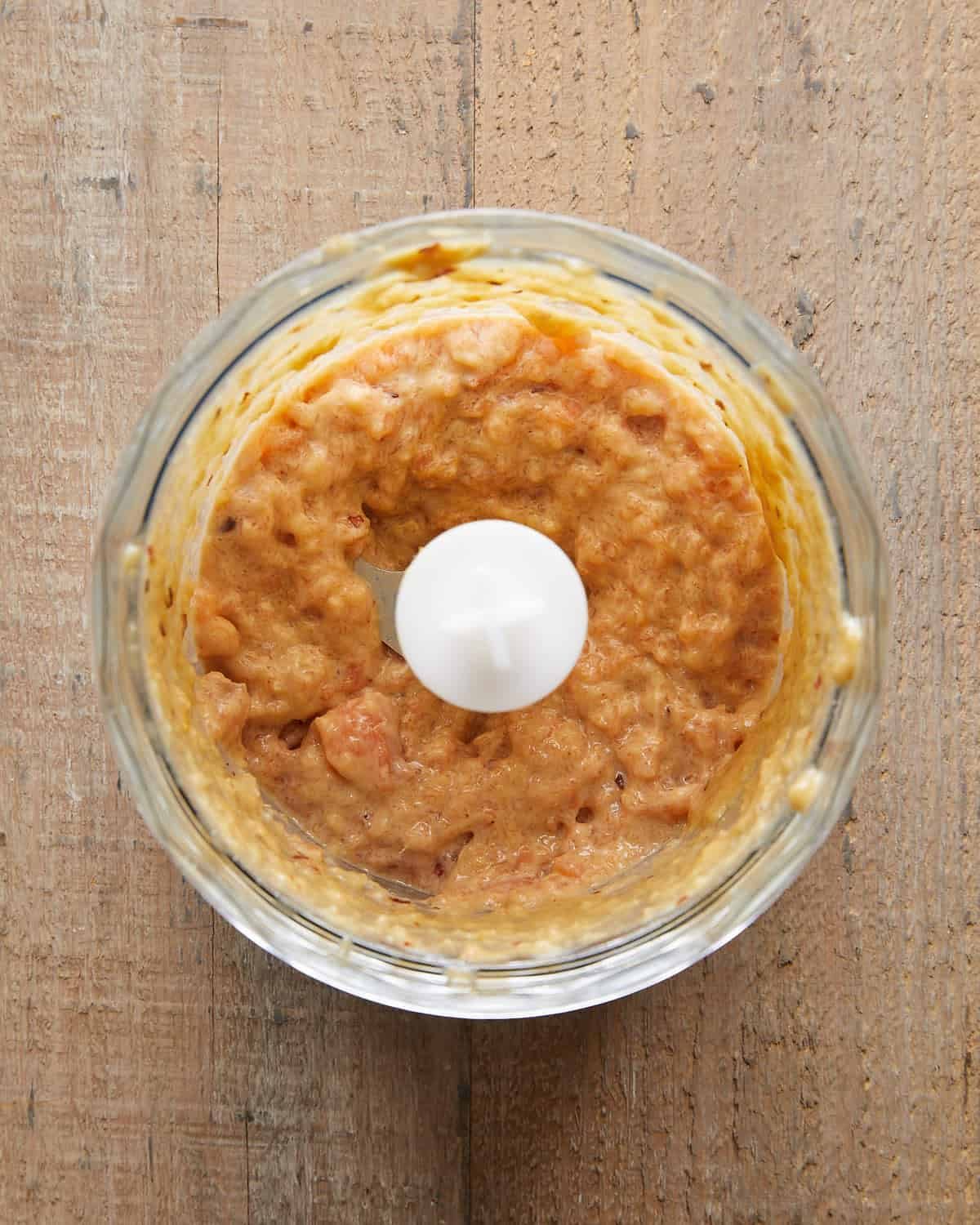 Overhead image of salmon mixture blended into a slightly chunky paste with green onions, garlic, and seasonings—ready to form into Asian salmon burgers for a flavorful, tender texture.