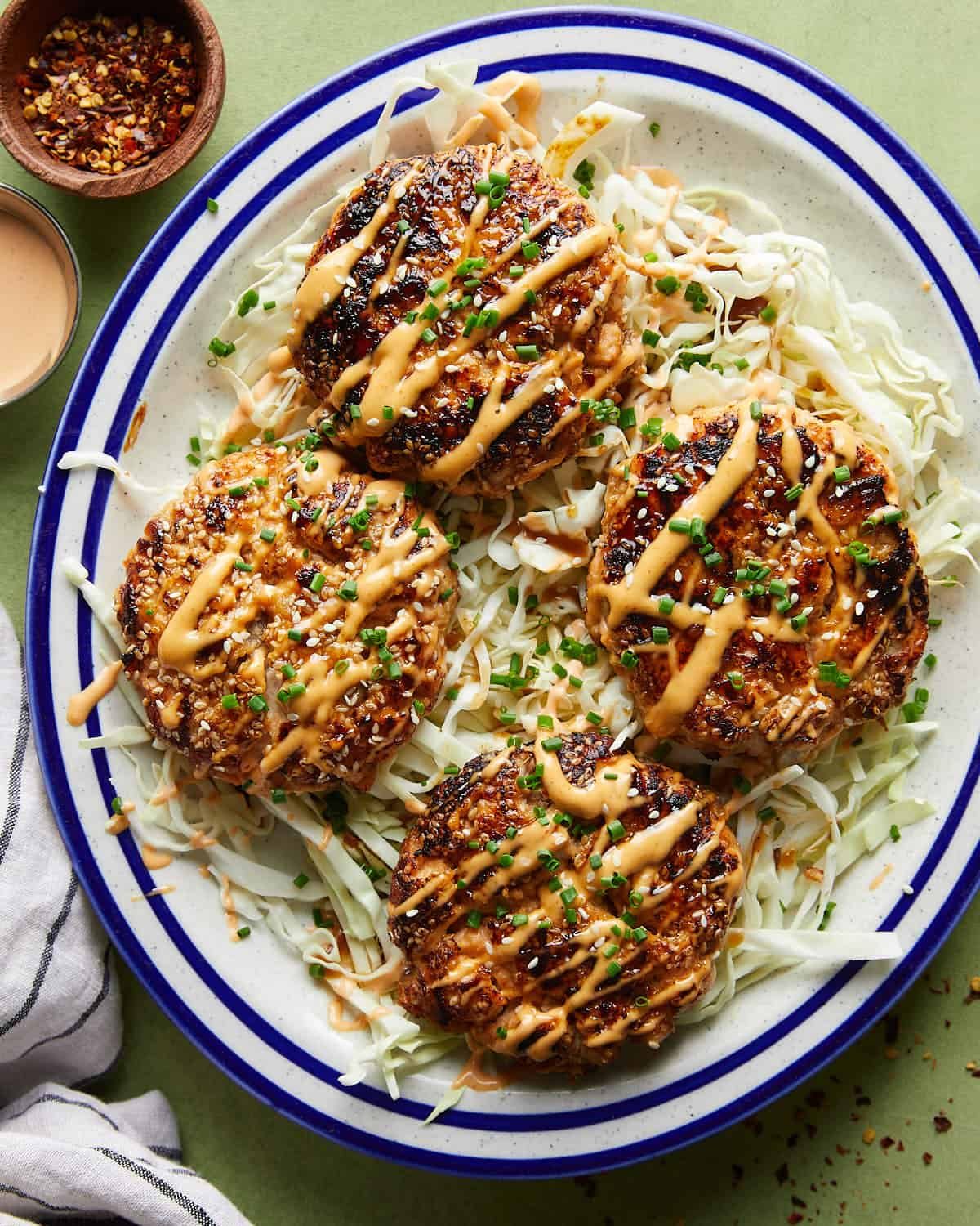 Overhead shot of juicy Asian salmon burgers served as patties over a fresh shredded cabbage bed, topped with herbs and sesame seeds.