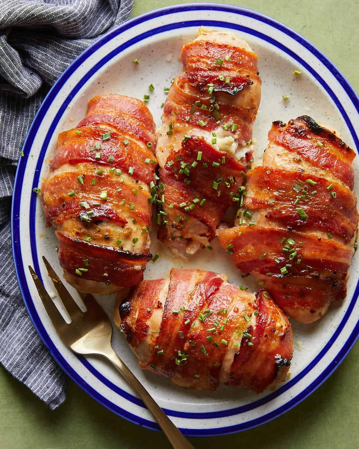 Overhead image of bacon wrapped stuffed chicken breasts with garnish on white dish with fork.