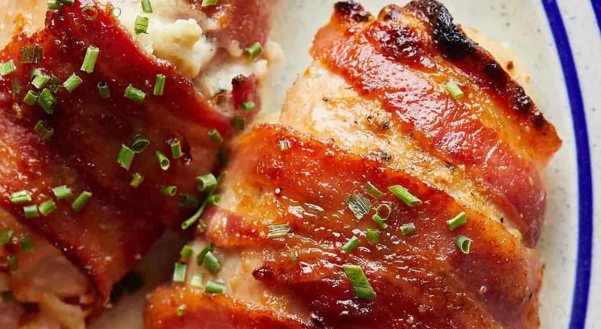 Overhead image of bacon wrapped stuffed chicken breast in the oven on white dish.