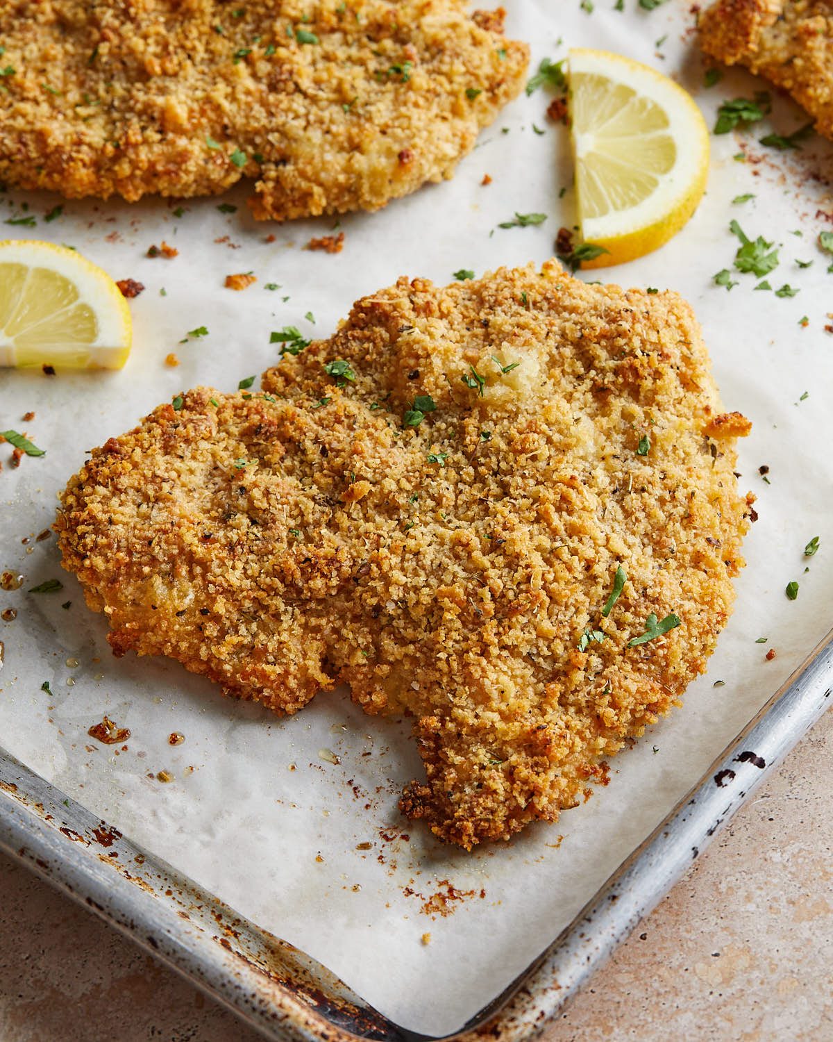 Close-up of crispy baked chicken cutlets with a golden panko-Parmesan coating, parsley, and lemon wedges.