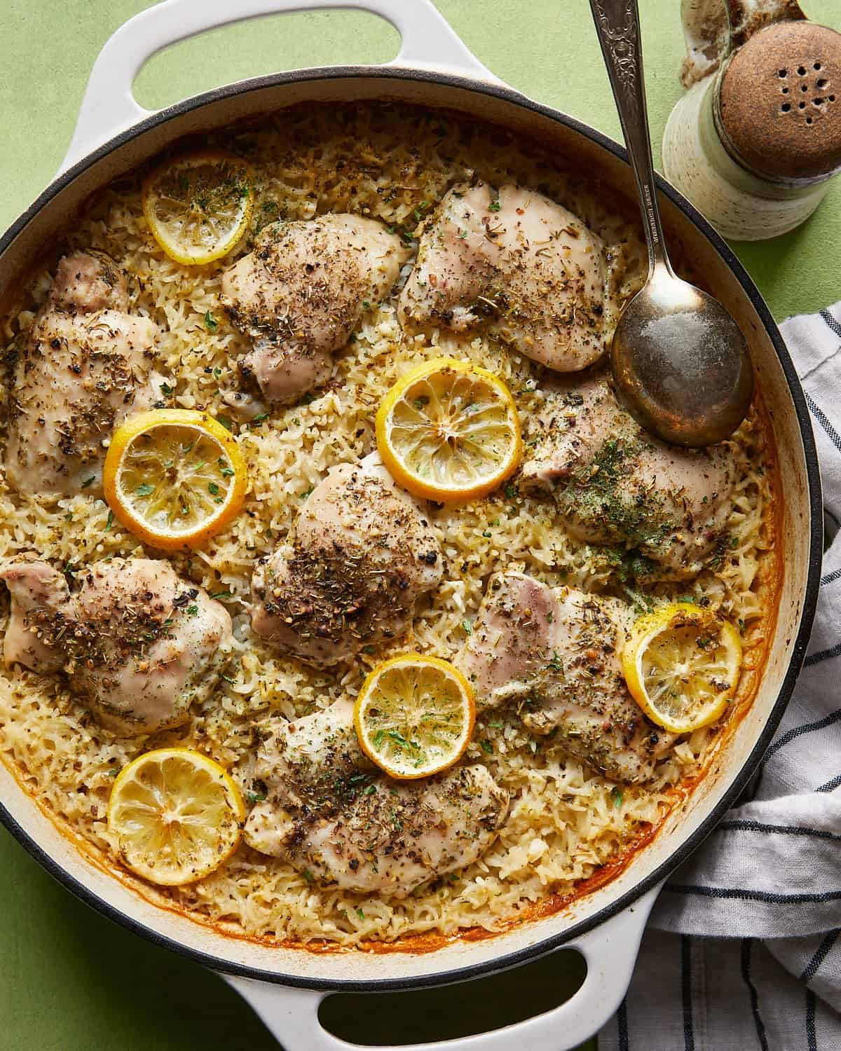 Overhead view of baked lemon chicken and rice with boneless chicken thighs, lemon slices, and basmati rice in a white braiser.