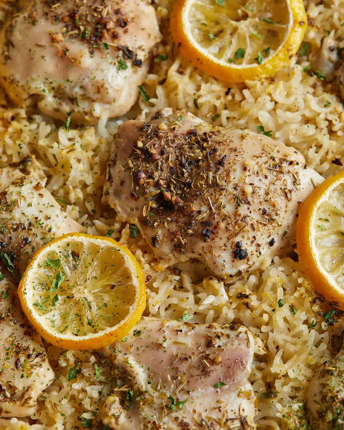 Close-up of boneless chicken thighs and basmati rice baked with lemon slices, garlic, and Italian seasoning.