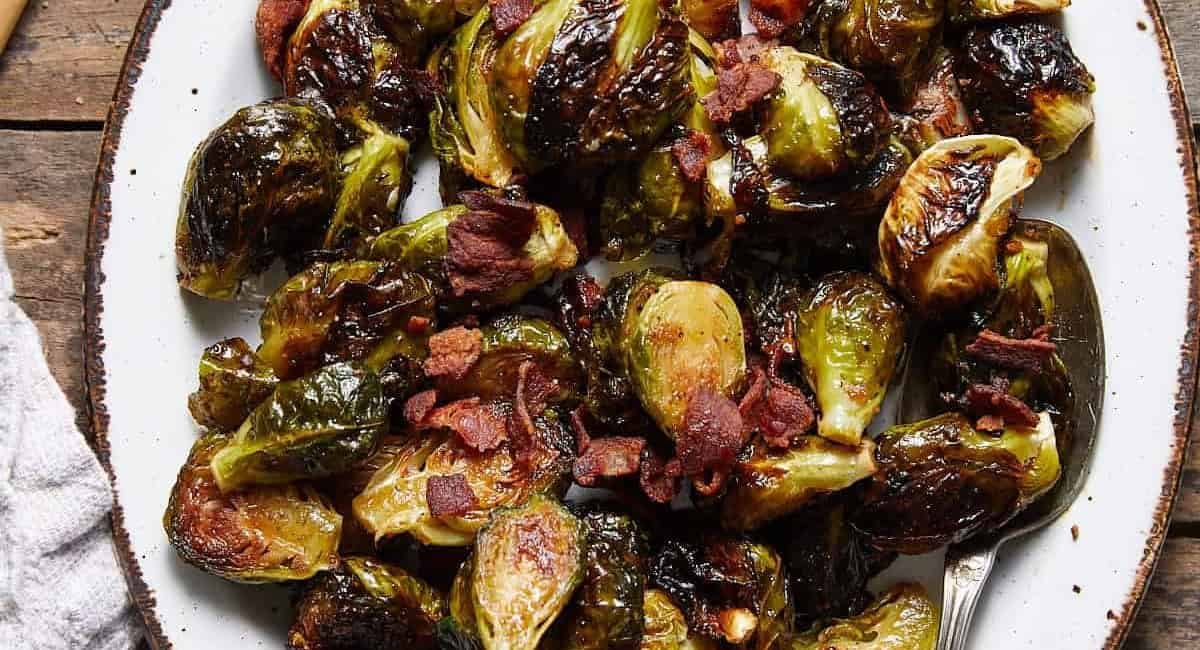 Overhead image of crispy glazed brussels sprouts with bacon on white dish.