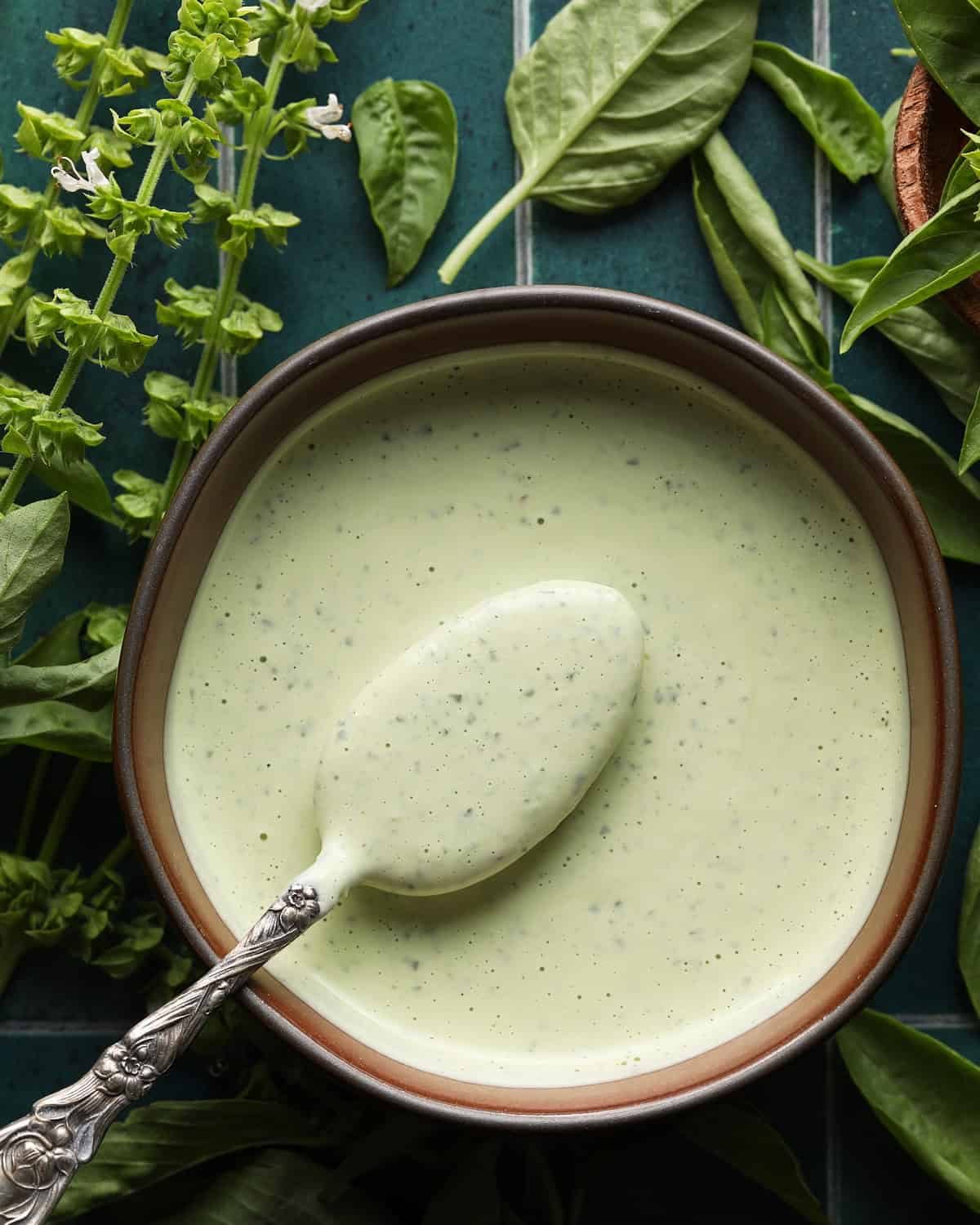 Bowl of creamy basil aioli with a spoon and fresh basil in the background.
