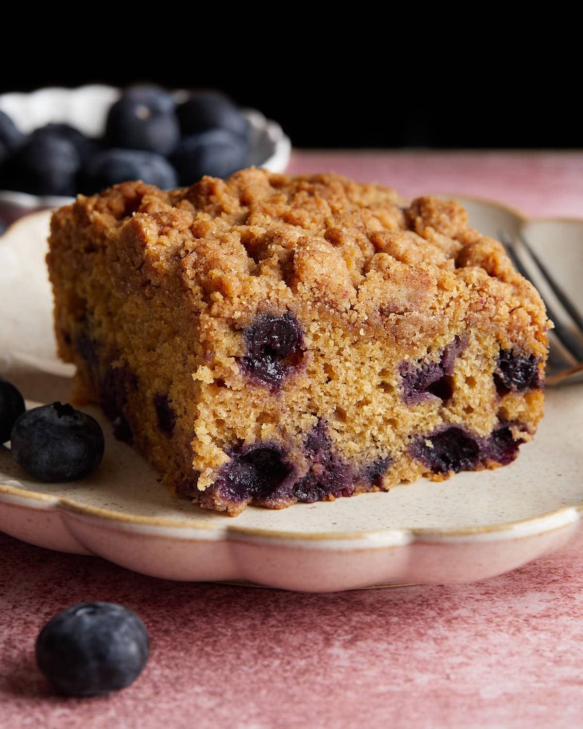 Side profile, up close image of blueberry coffee cake on white plate.