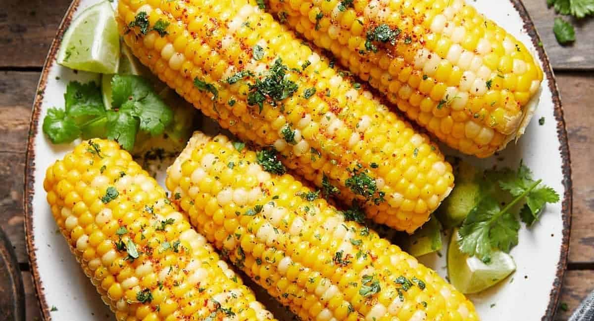 Overhead image of chili lime corn on the cob with garnish on white dish.