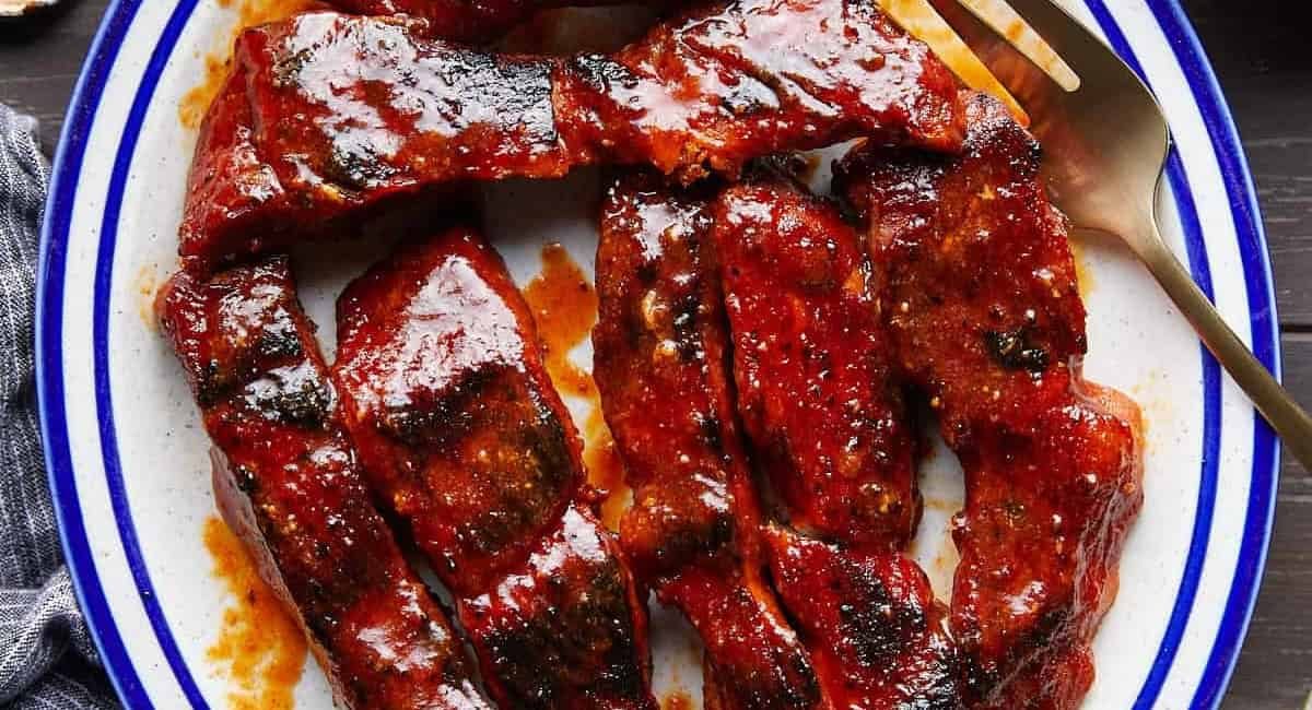 Overhead image of boneless pork ribs in the oven on white and blue plate with fork on the side.