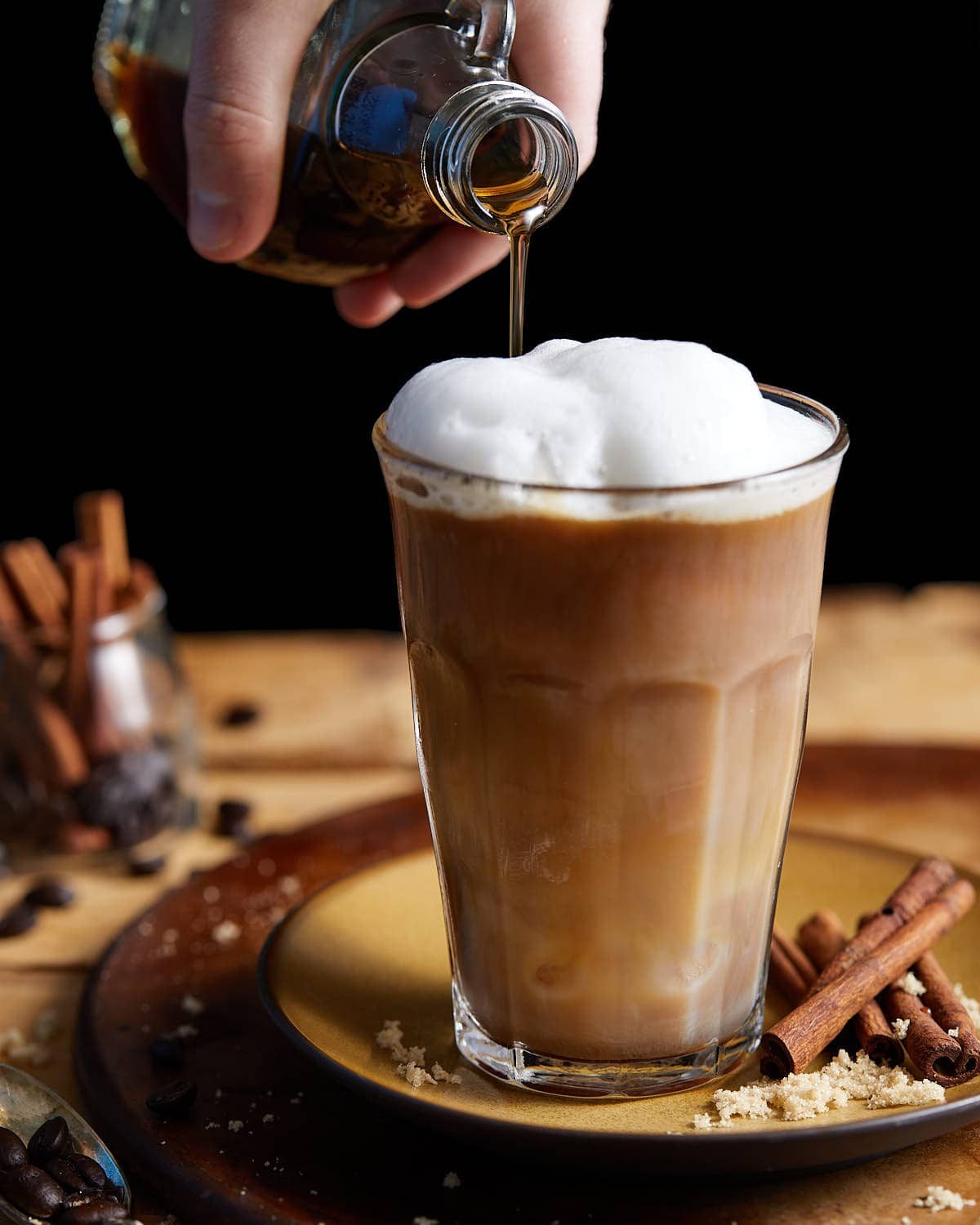 Brown sugar syrup being poured into coffee.