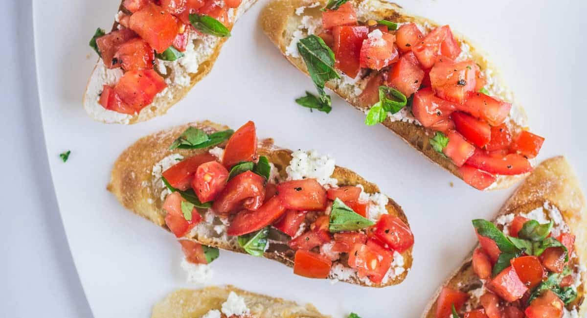 Overhead image of bruschetta with marinated feta on white dish.