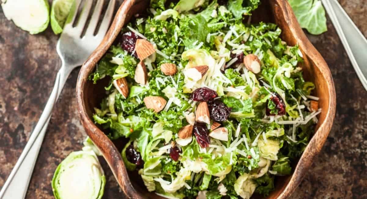 Overhead image of kale brussel sprouts salad with honey mustard dressing in brown bowl.