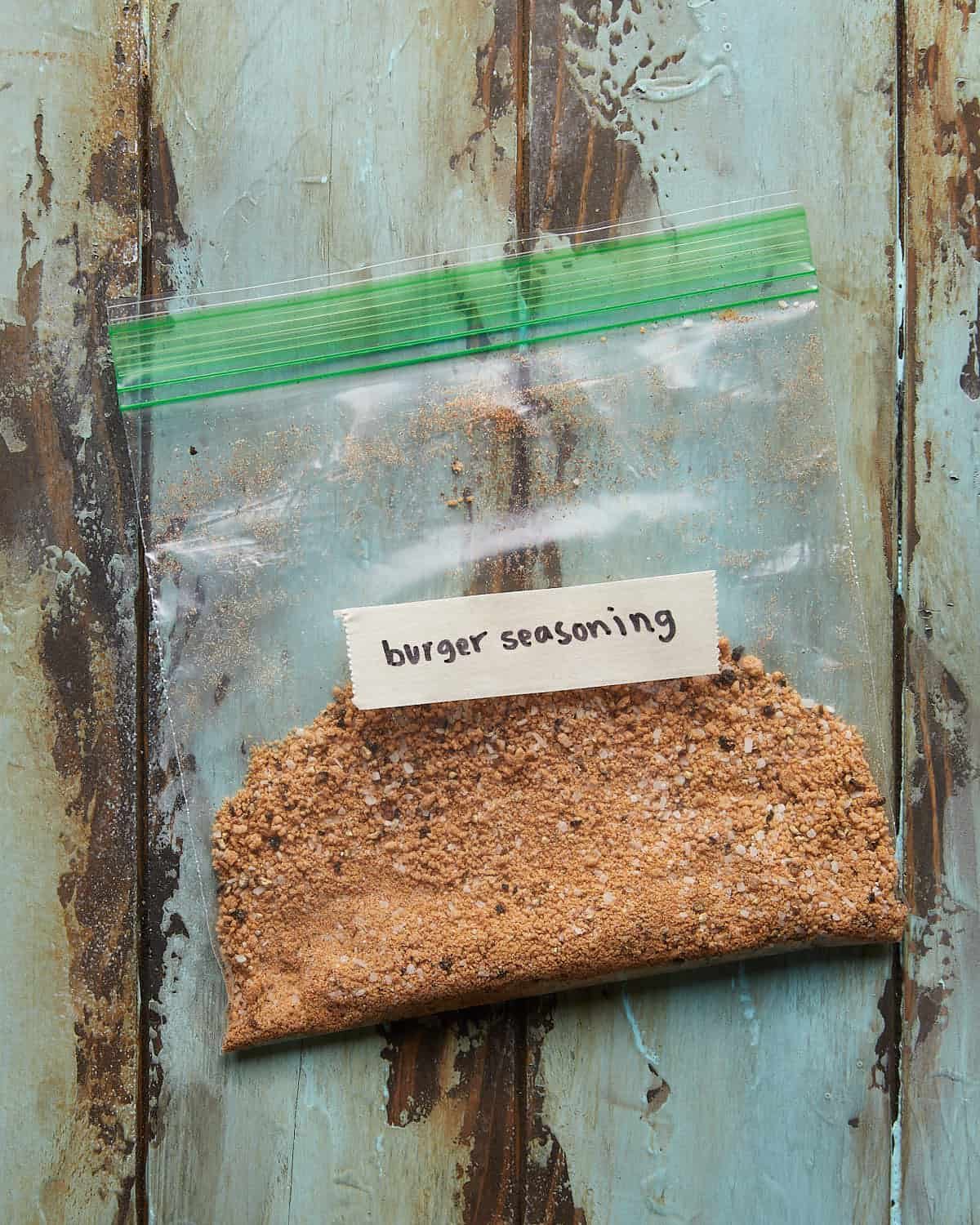 Overhead photo of a small bag of burger seasoning on a green wooden background.