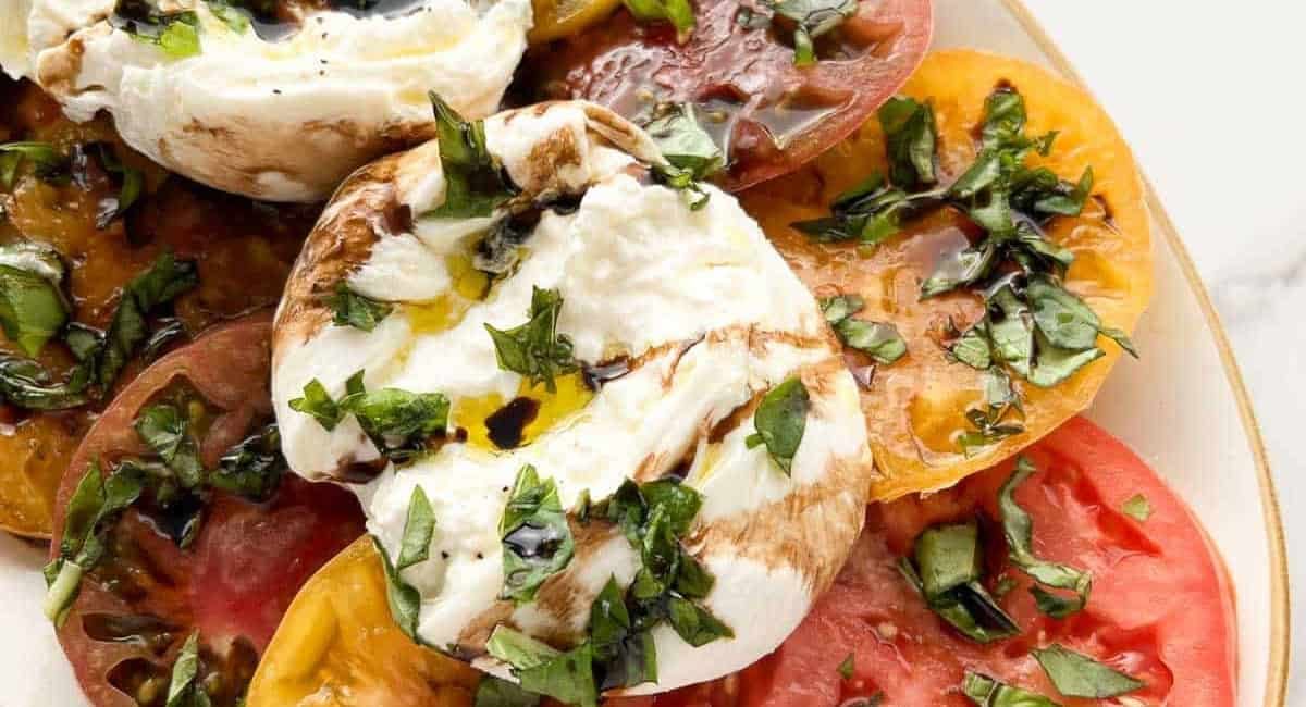 Overhead image of burrata caprese with fresh herbs on top.