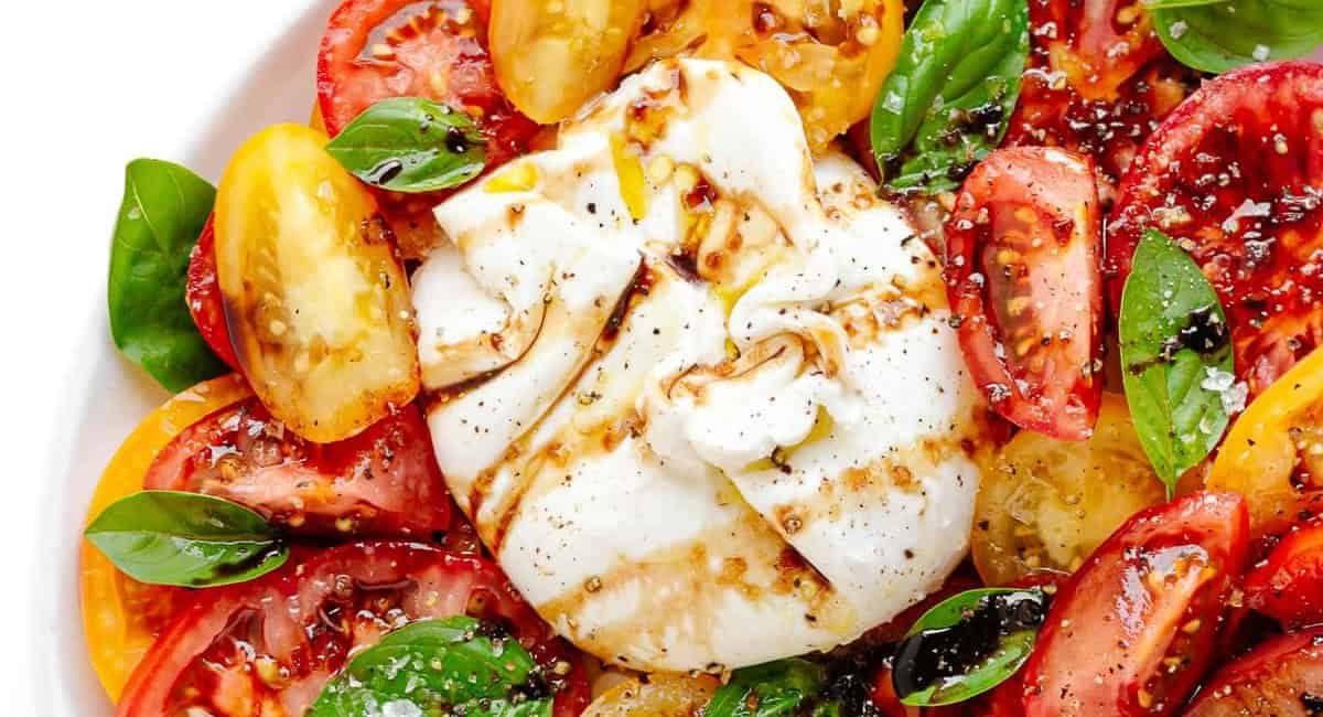 Overhead up close image of burrata Caprese on white dish.