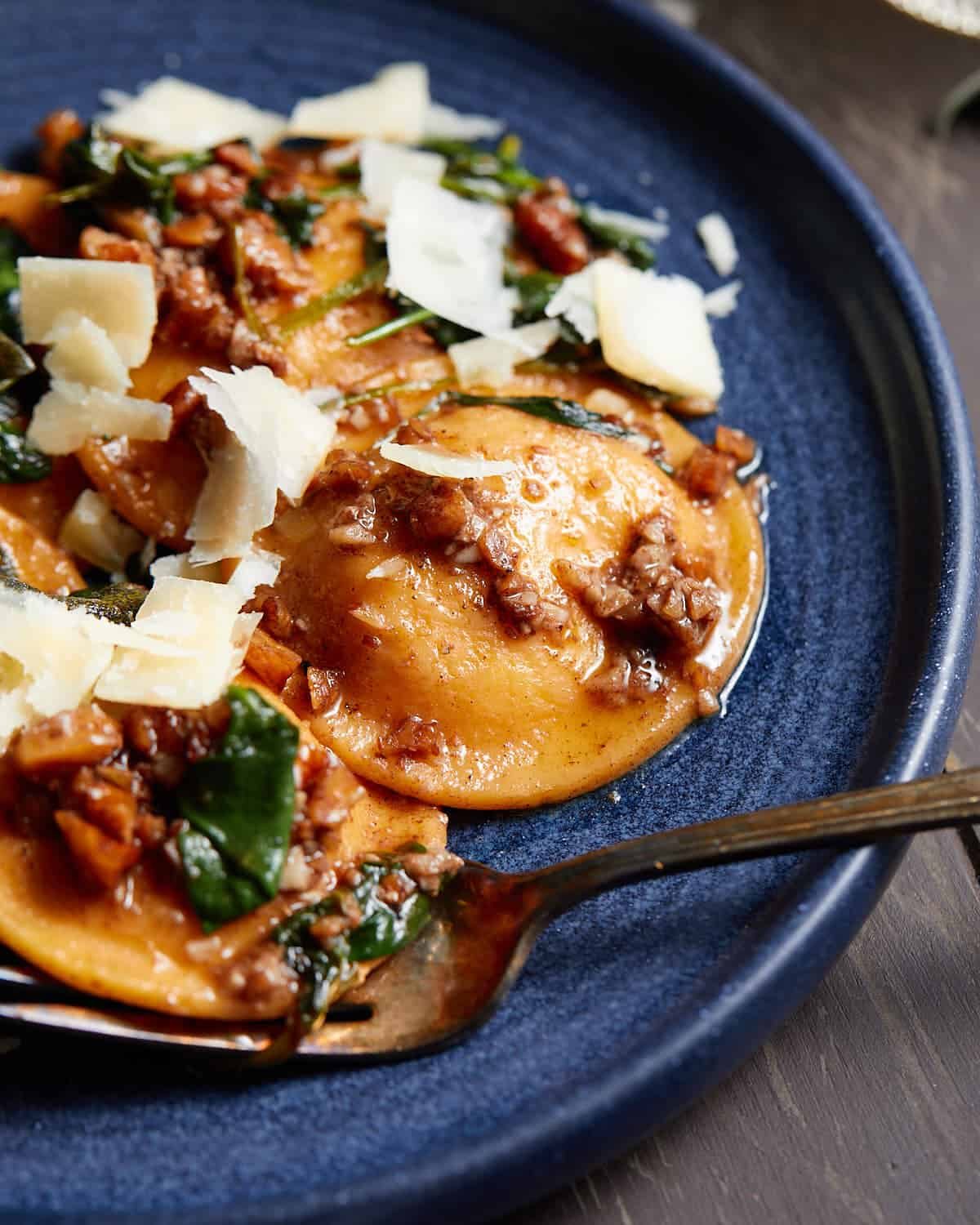 Up close image of butternut squash ravioli sauce on blue dish with garnish.