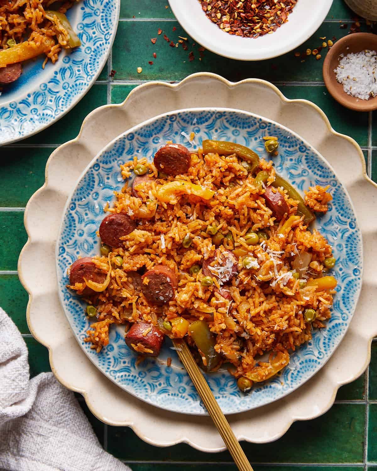 Cajun sausage and rice with bell peppers, peas, and grated Parmesan on a blue-and-white plate.