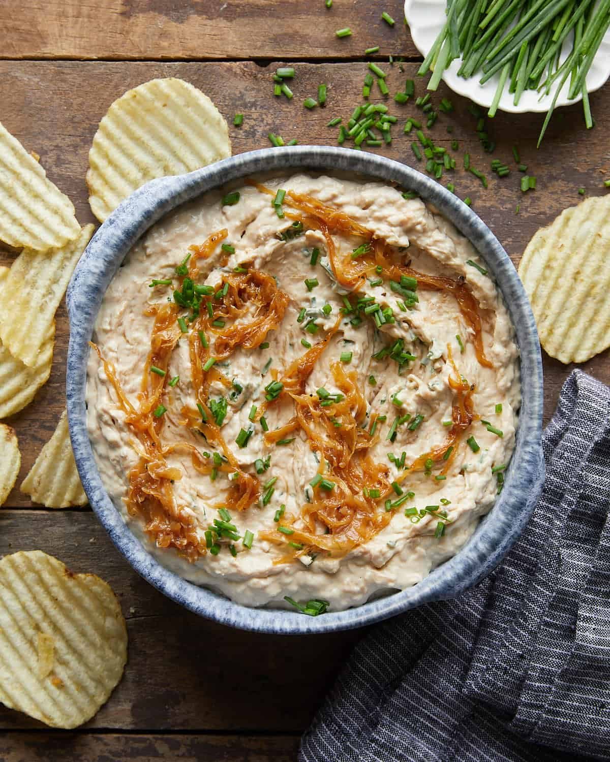 Overhead image of homemade caramelized french onion dip with garnish and potato chips.