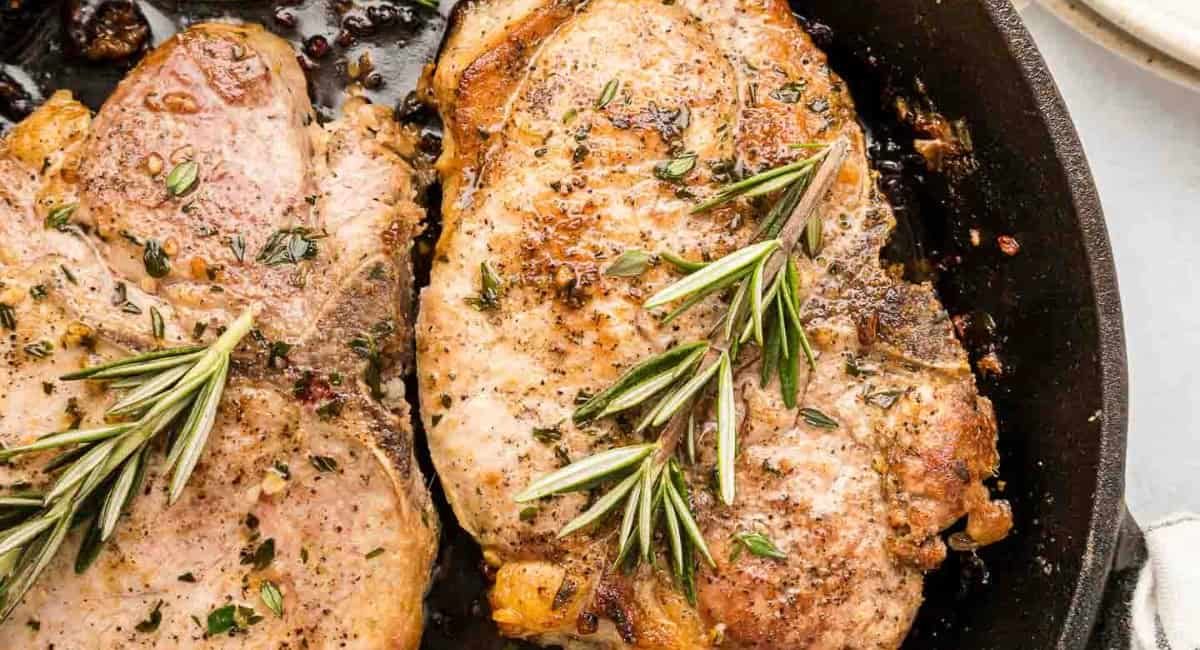 Overhead image of cast iron skillet pork chops with rosemary garnish.