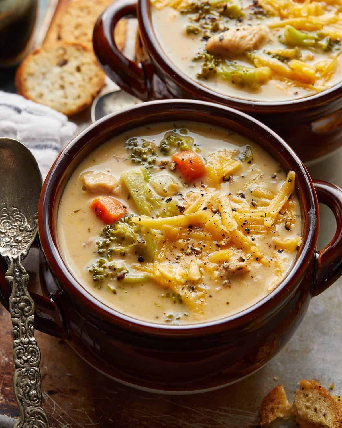 Up close and overhead image of chicken broccoli cheddar soup in brown bowl with garnish.
