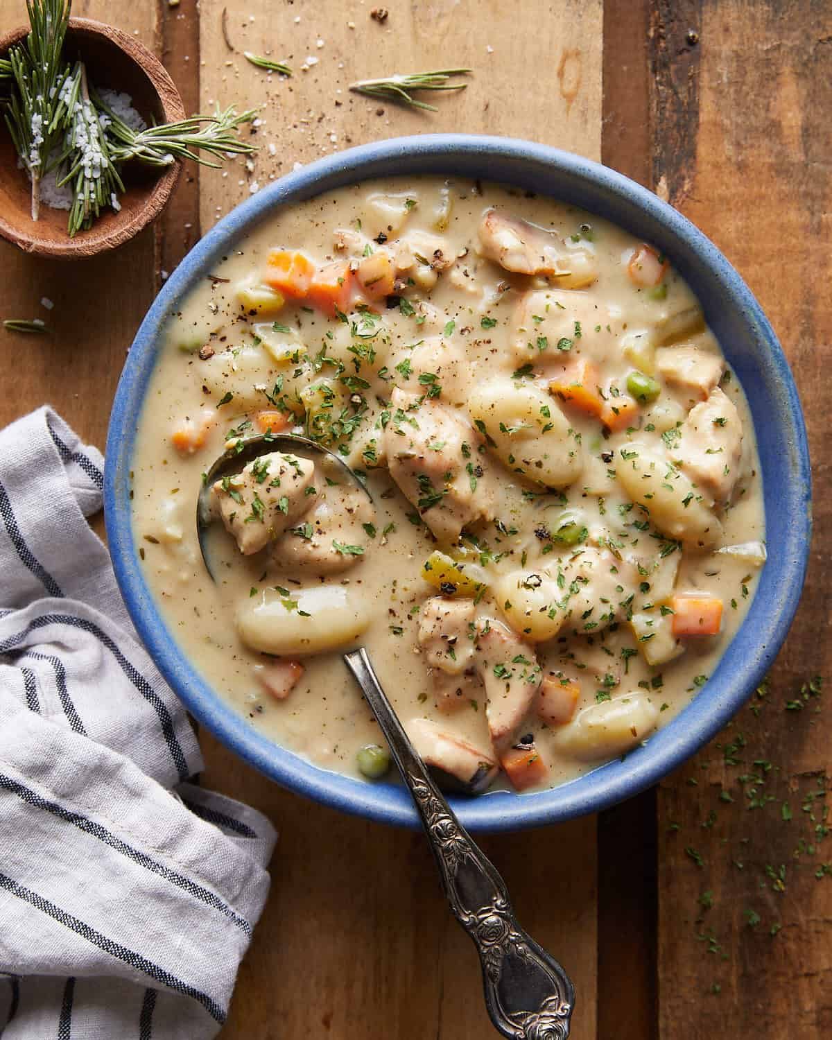 Overhead image of chicken and dumplings with gnocchi in blue bowl with silver spoon.