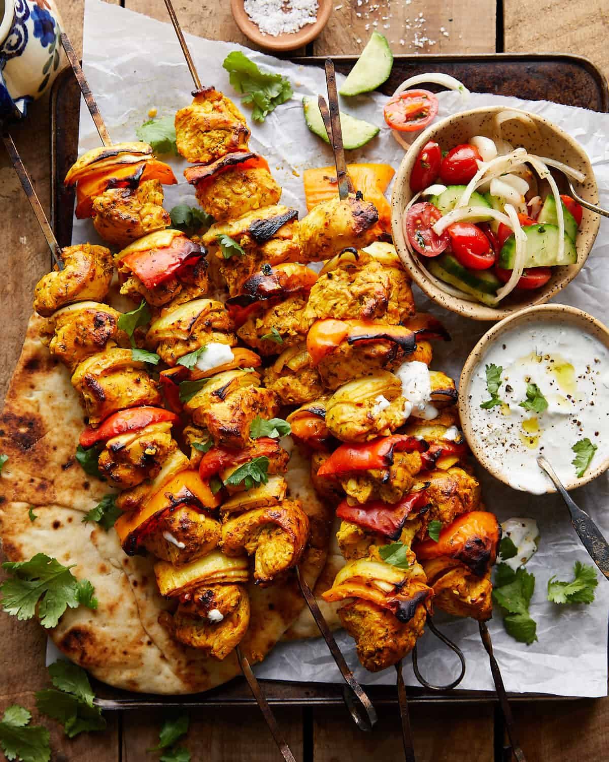 Overhead image of chicken kabobs with garnish and dips on the side.