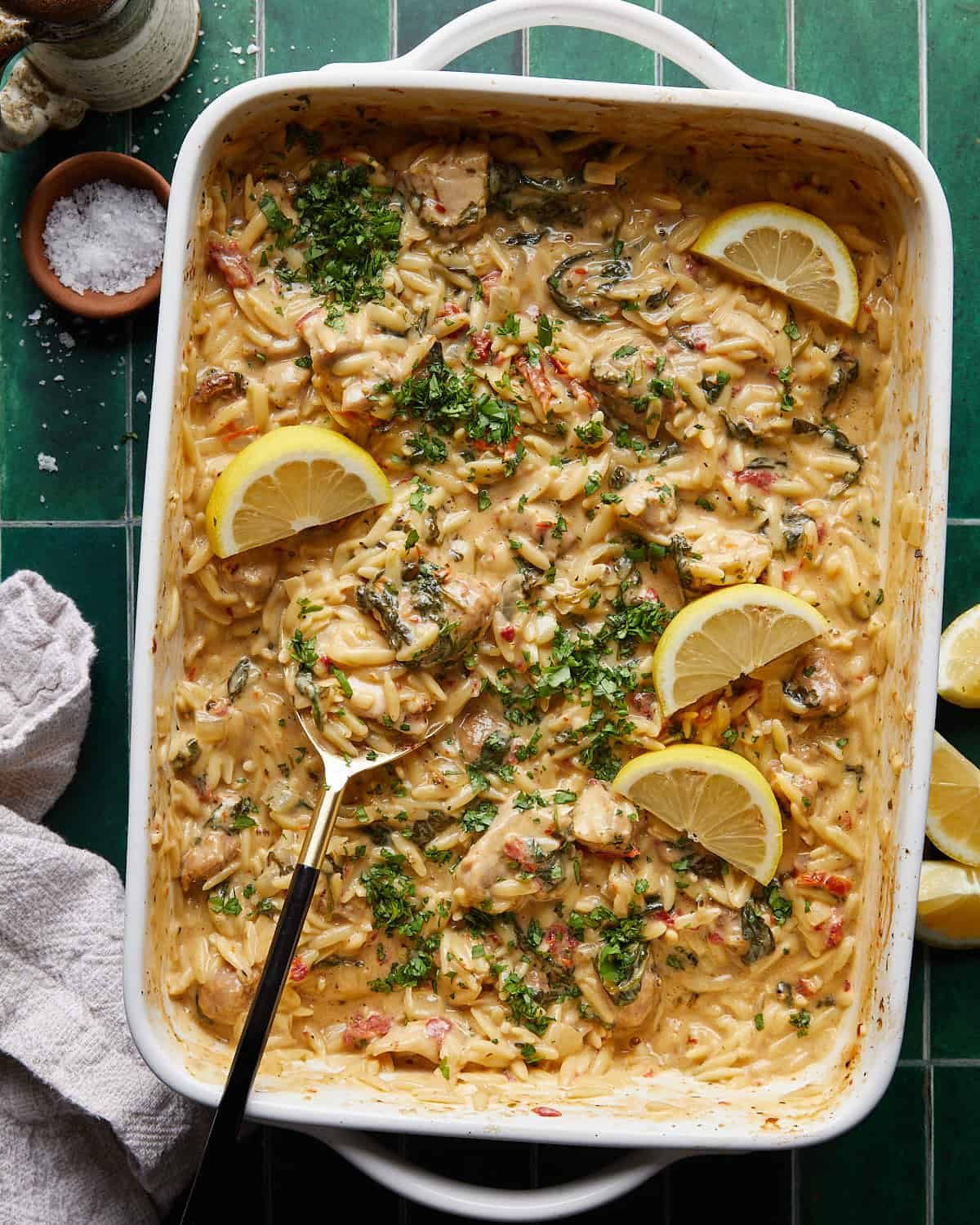 Overhead image of chicken and orzo bake in white baking dish with garnish.
