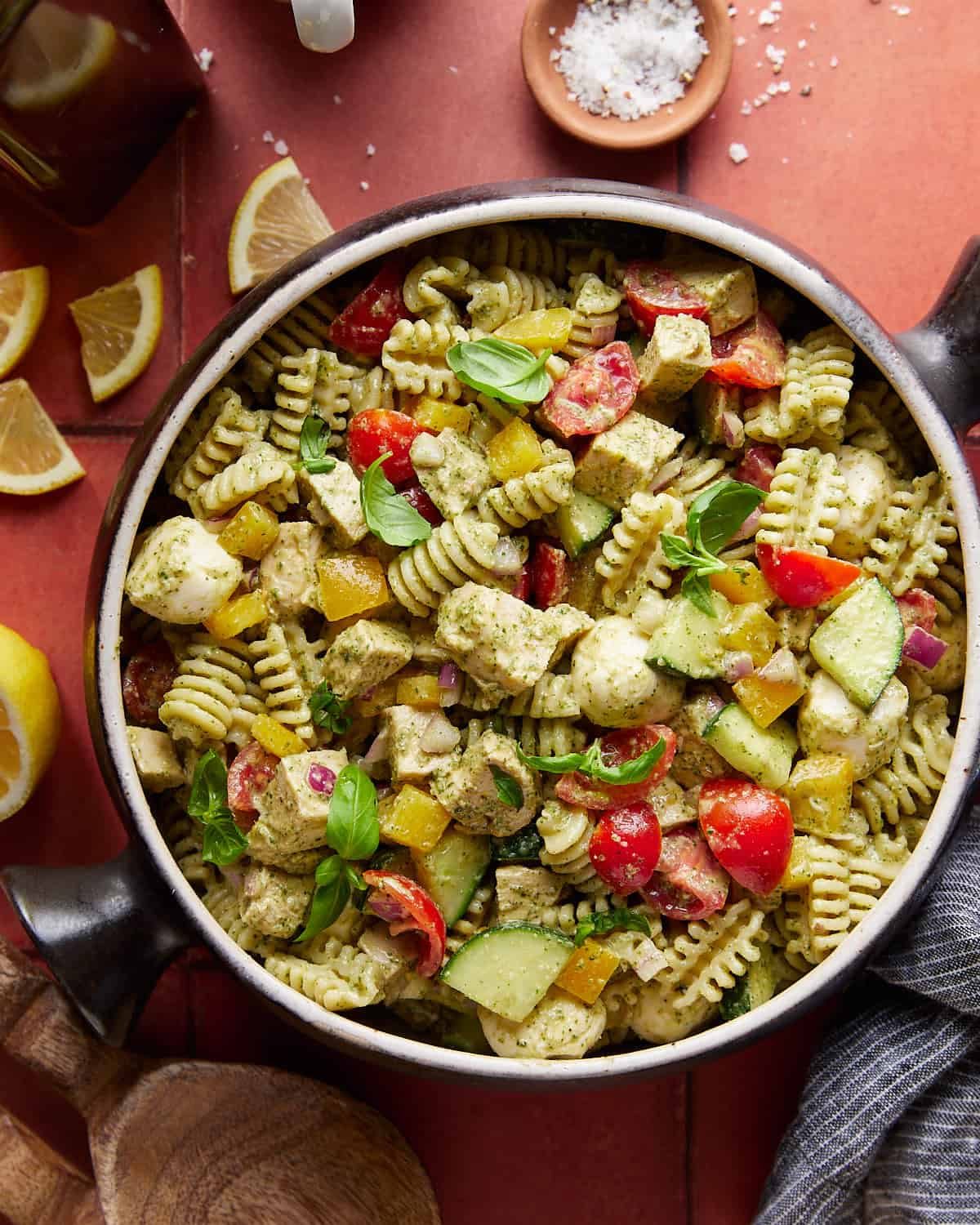 Overhead image of chicken pesto pasta salad with garnish in bowl.