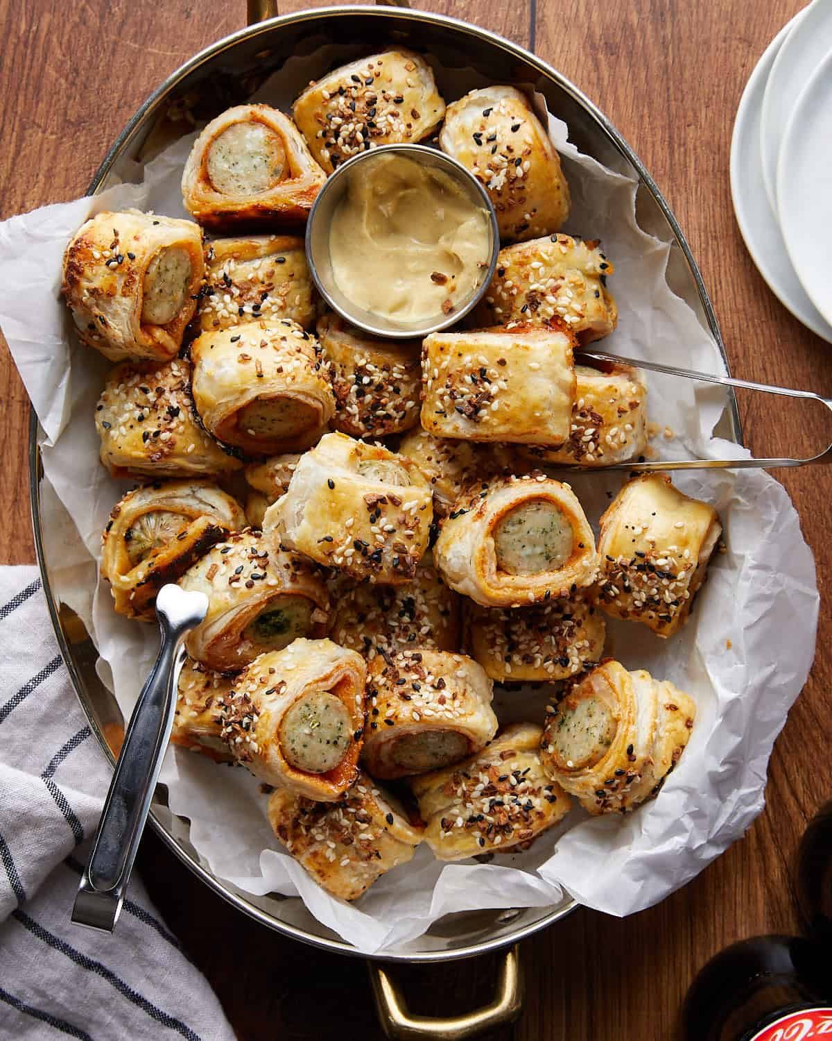 Overhead image of chicken sausage rolls in metal plate with dipping sauce on the side.