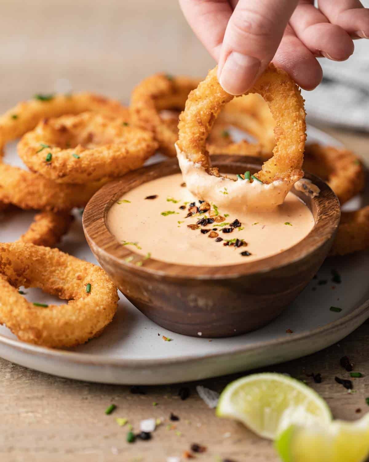 Onion ring being dipped in easy chipotle crema.