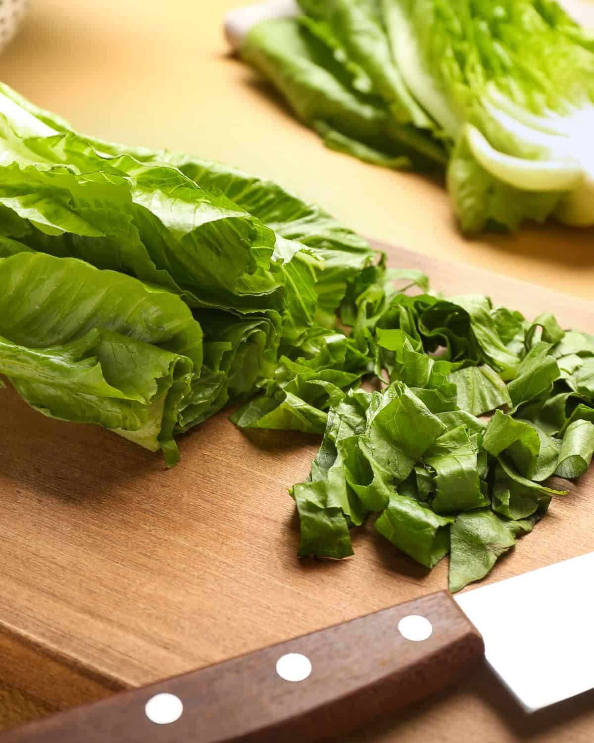 Up close photo of cutting romaine lettuce on wooden cutting board.