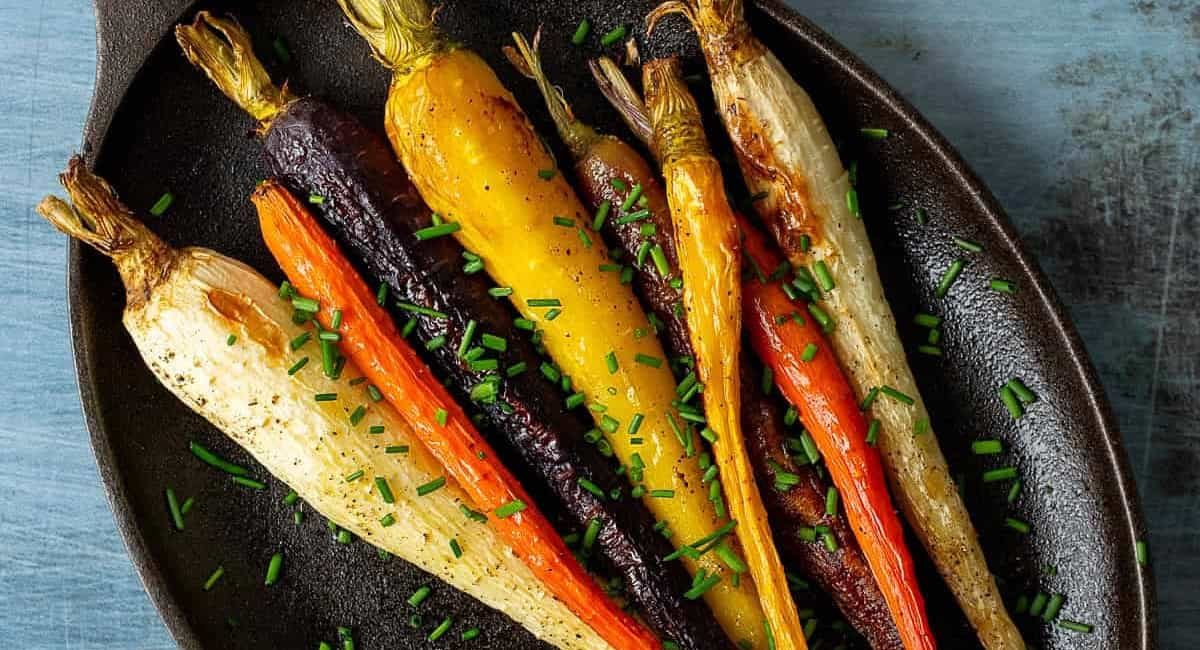 Overhead image of roasted rainbow carrots with garnish on black plate.