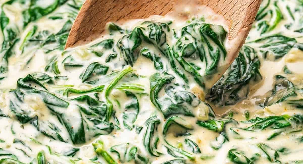 Up close image of creamed spinach being shown with wooden spoon.
