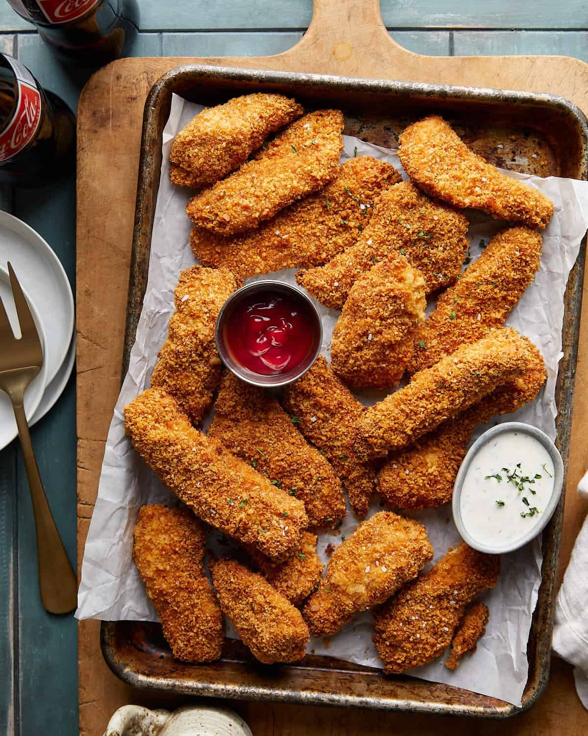 Golden baked chicken tenders with panko coating, ketchup, and ranch on a sheet pan.