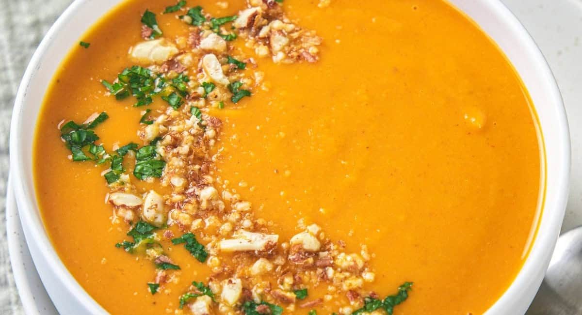 Overhead up close image of Thai curried pumpkin soup with garnish in white bowl.