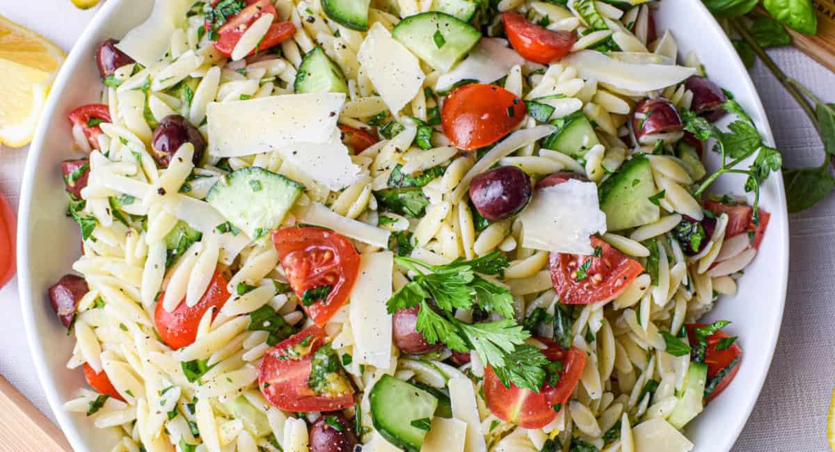 Overhead image of lemon orzo salad with garnish in white bowl.