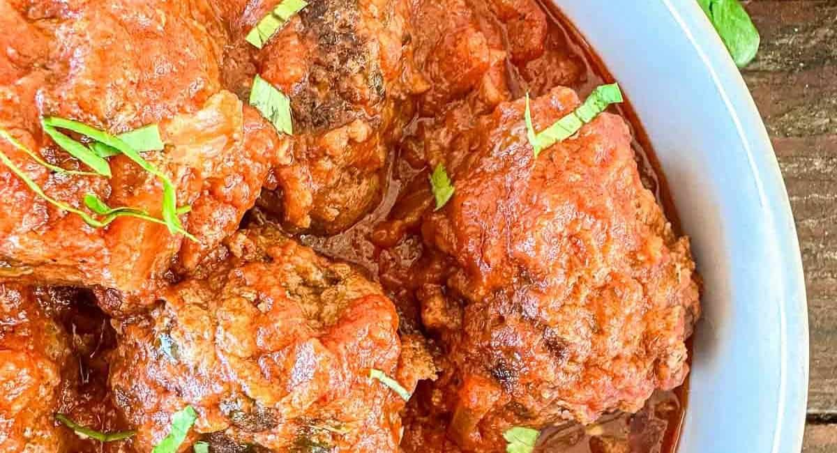 Overhead up close image of dutch oven meatballs in tomato sauce with garnish.