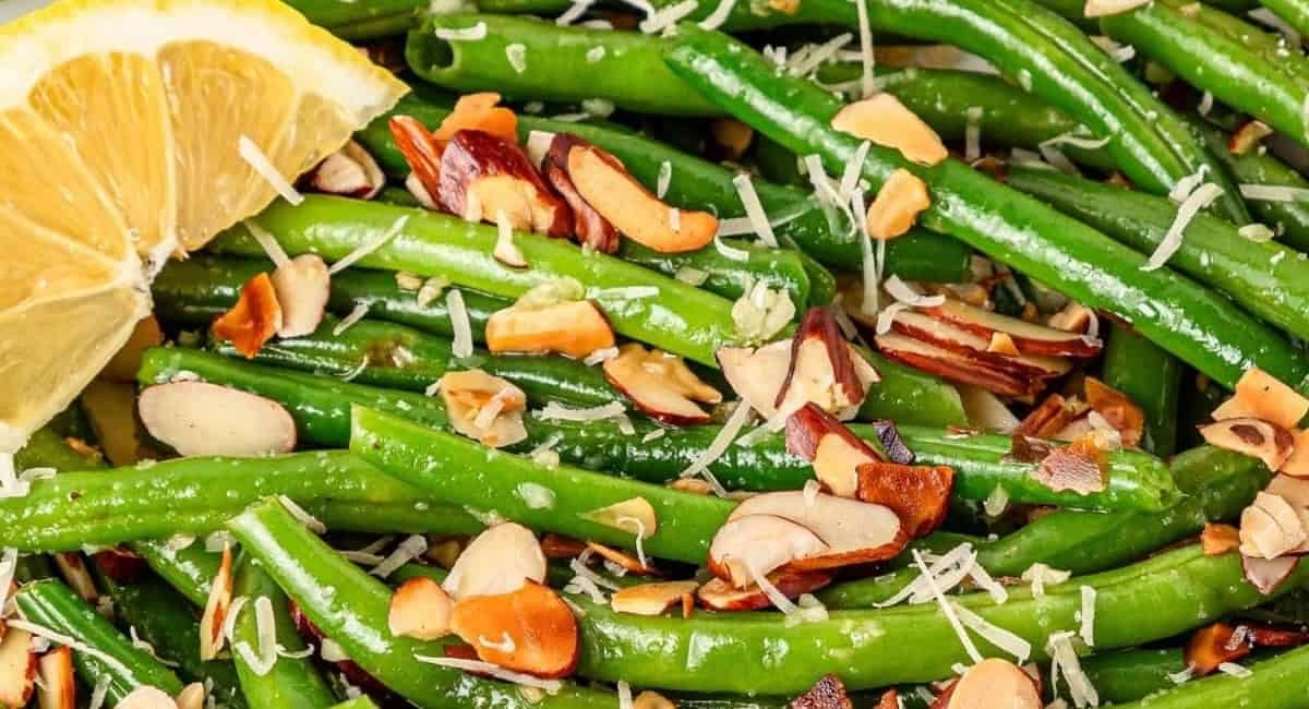 Up close overhead image of green beans almondine with garnish and lemon slice.